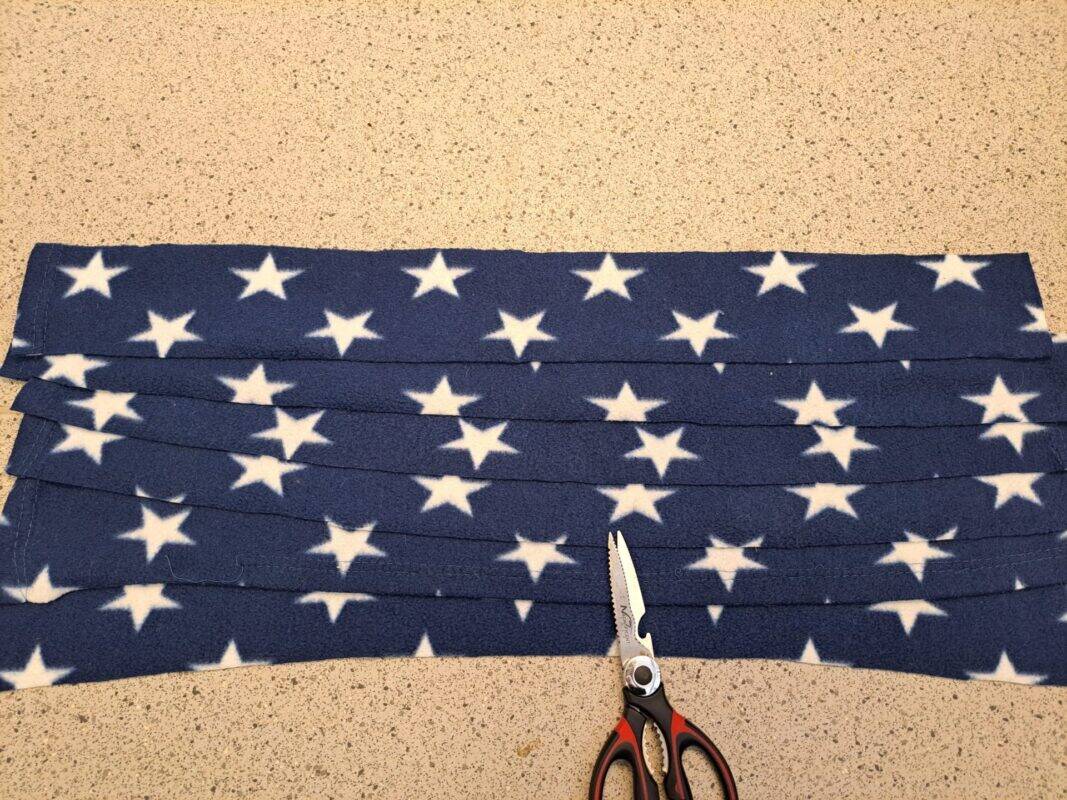 A pair of scissors rests next to strips of blue fabric with white stars, arranged neatly on a speckled countertop—perfect materials for crafting a cozy rat hammock.