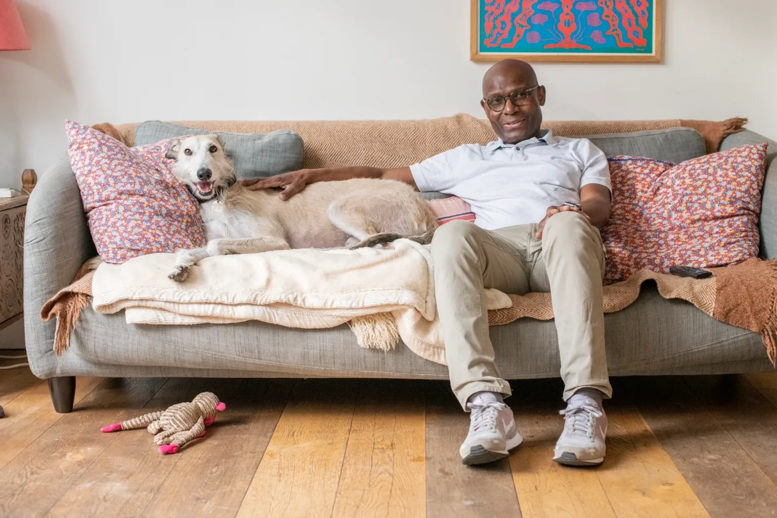 A man sitting on the living room sofa with his dog lying down next to him