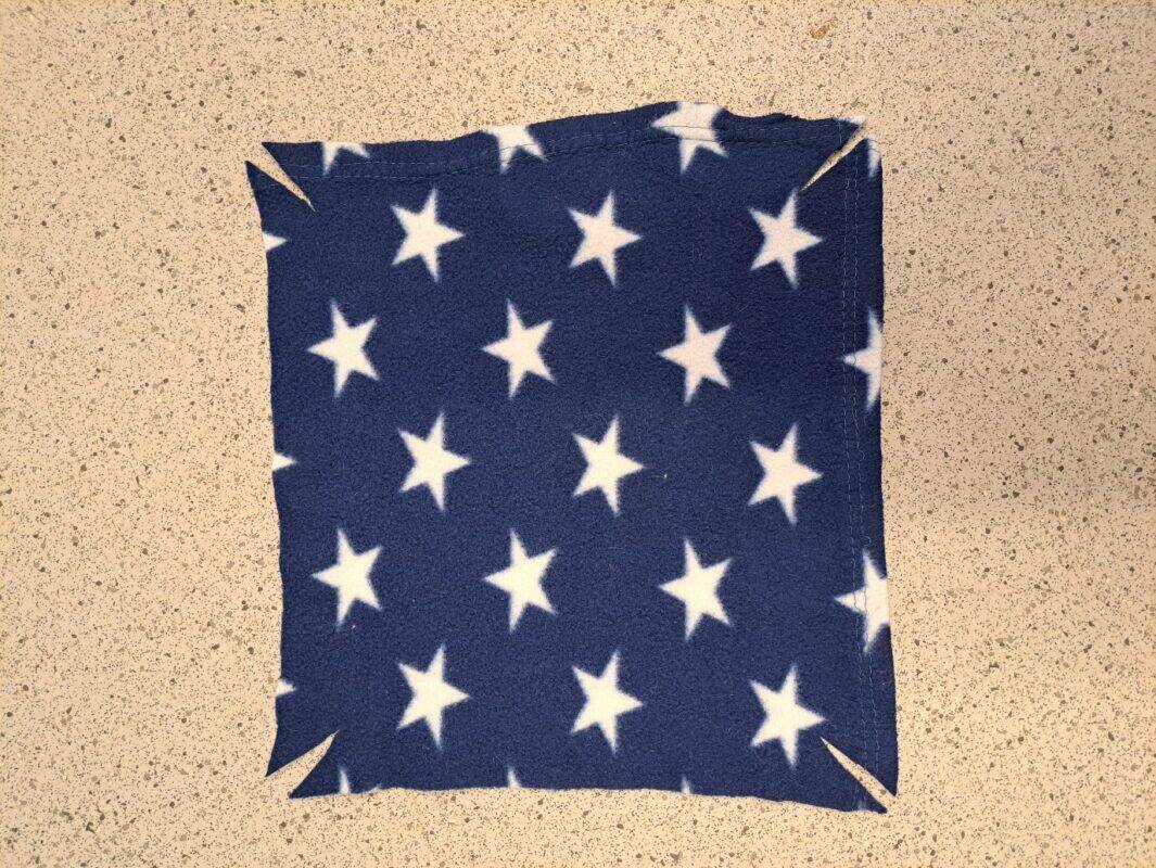 A square rat hammock of dark blue fabric with white stars rests on a speckled surface. Each corner of the hammock features a short diagonal cut.