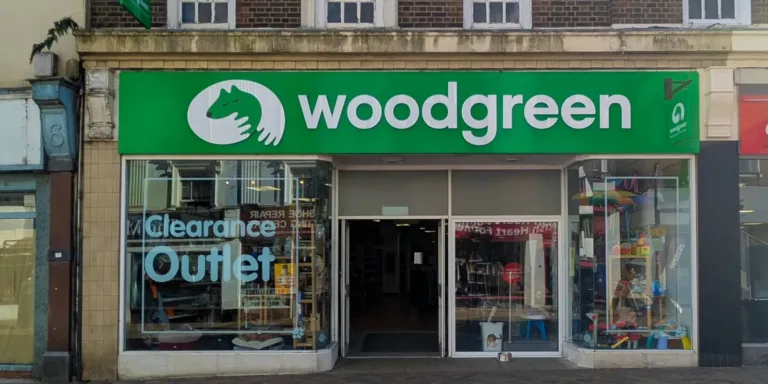 The storefront of Woodgreen Clearance Outlet, a Banbury charity shop, features a green sign with a white logo of a dog and cat above the entrance, and displays Clearance Outlet in bold letters in the left window.