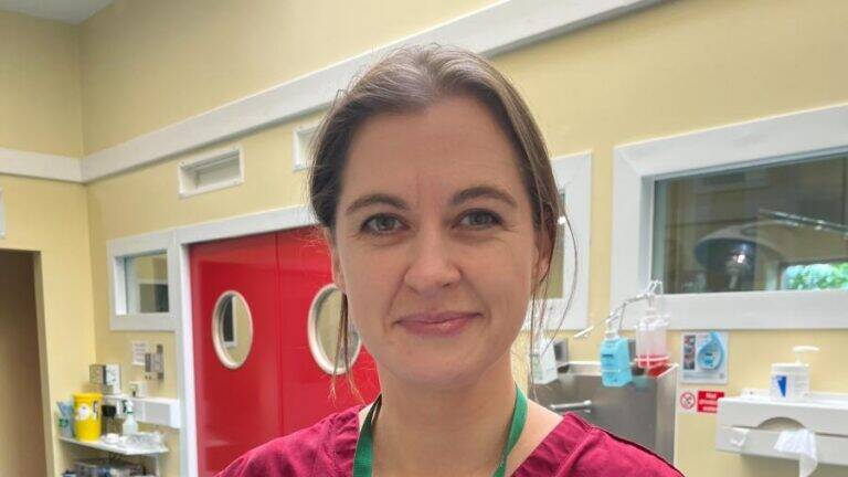 A woman wearing a maroon scrub top and a green lanyard stands in a medical surgery.