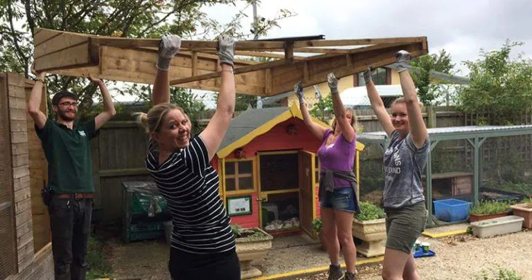 Four volunteers smiling at the camera, whilst working on some pet home construction at Woodgreen's pet care centre in Godmanchester, Cambridgeshire