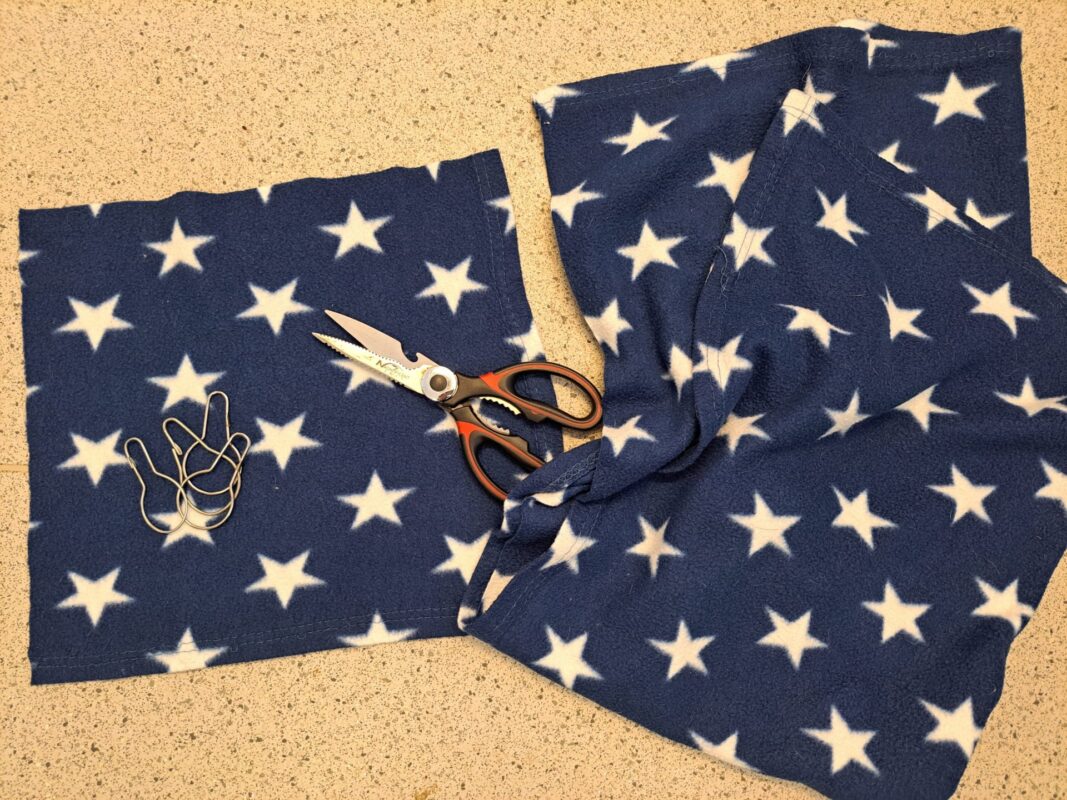 A pair of scissors, a piece of blue fabric with white stars—perfect for crafting a cozy rat hammock—and several shower hooks are arranged on a speckled countertop.