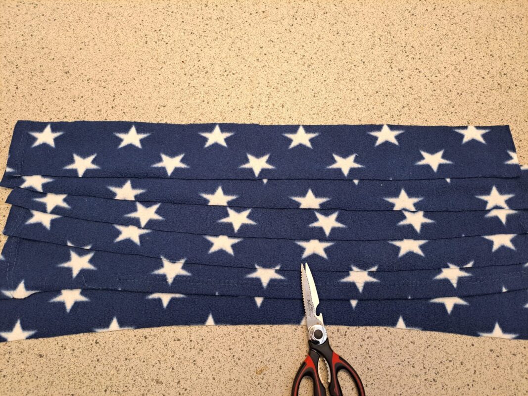 A pair of scissors rests next to strips of blue fabric with white stars, arranged neatly on a speckled countertop—perfect materials for crafting a cozy rat hammock.