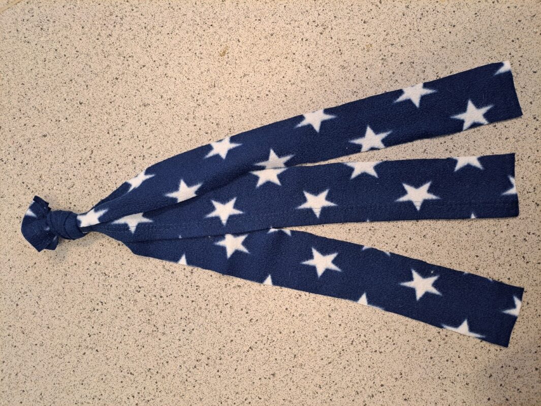 A piece of dark blue fabric with white stars, tied in a knot at one end, forms a cozy rat hammock with three long strips hanging down, placed on a speckled countertop.