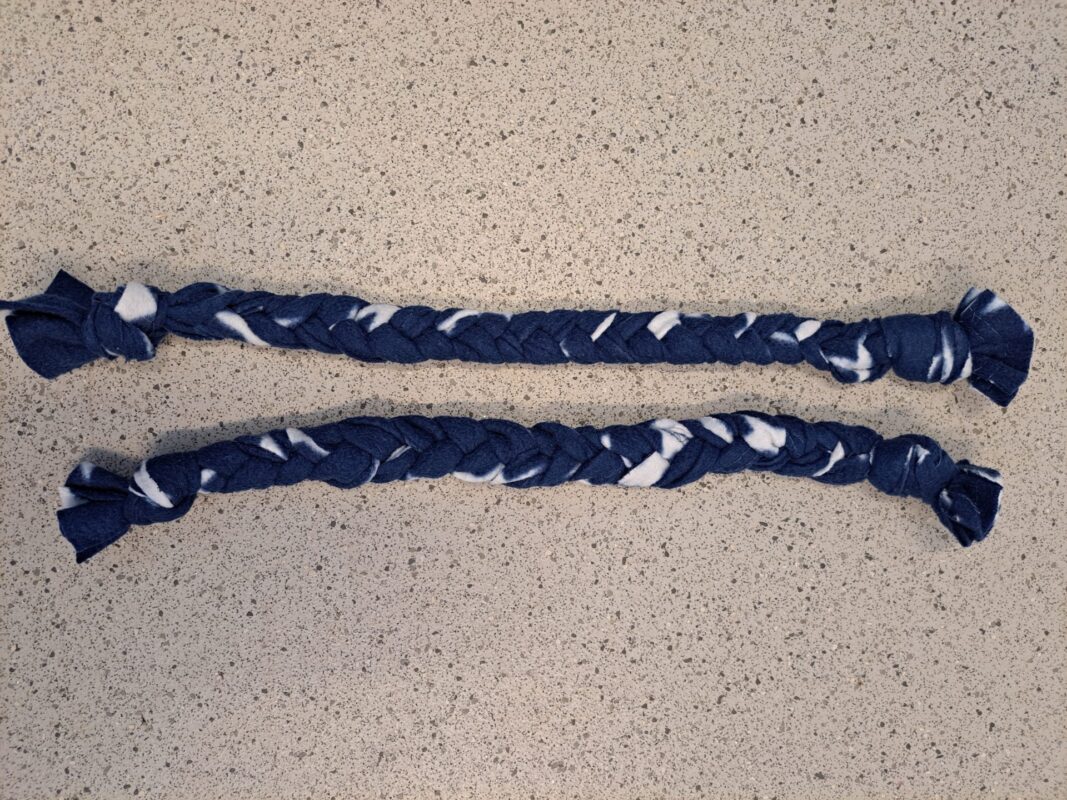 Two braids crafted from dark blue and white fleece fabric, lie side by side on a speckled countertop next to a cozy rat hammock.