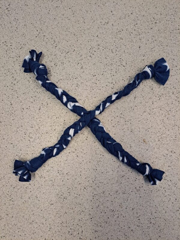 Two blue and white braided fabric strips, perfect for crafting a cozy rat hammock, are arranged in an X shape on a speckled light gray countertop.