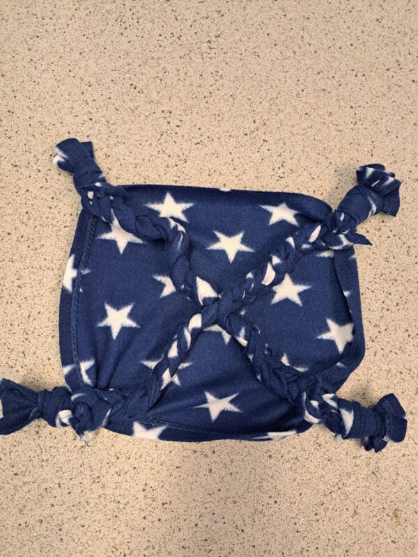 A rectangular piece of blue fabric with white stars, tied at the corners and in the middle to form a rat hammock pouch with knotted sections, lies on a speckled countertop.