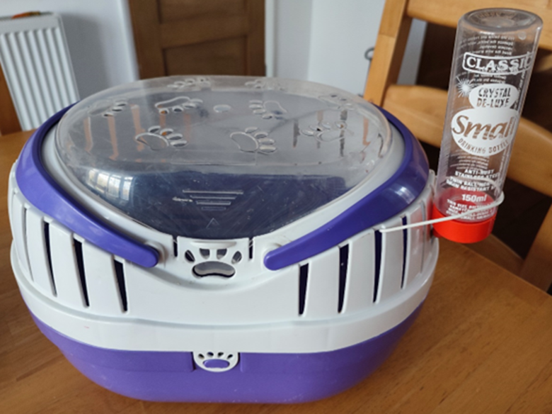 A purple and white pet carrier with a clear lid and attached water bottle.