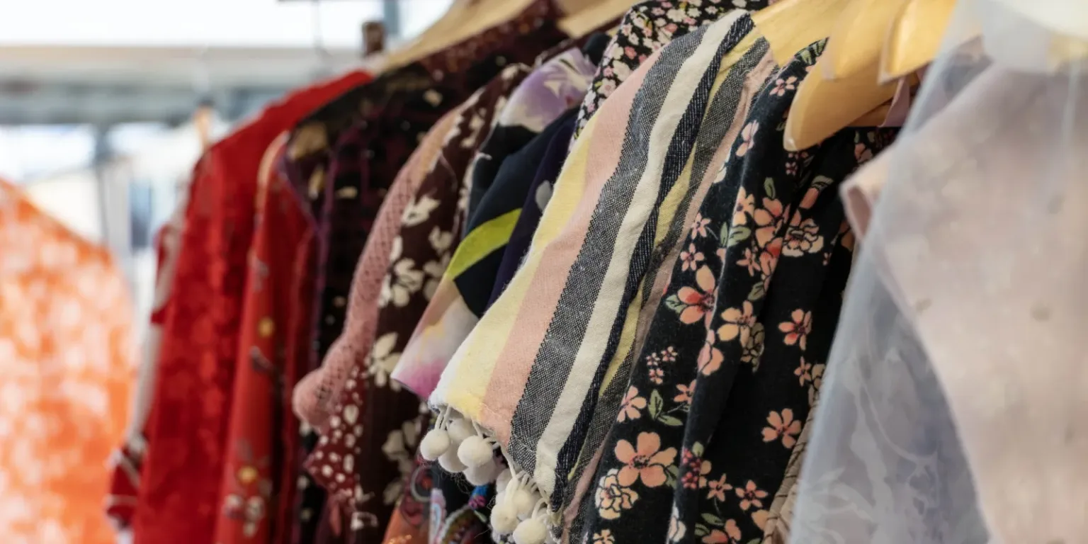 A close-up view of colorful dresses with floral and striped patterns hanging on wooden hangers in a row.