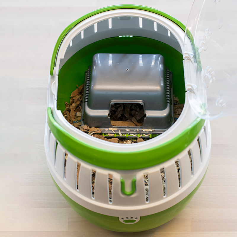 A top-down view of a green and white carrier for mice with a transparent lid, containing bedding material and a small plastic hideaway box inside.